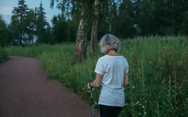 Elderly woman practicing Nordic walking on a park trail, promoting health and fitness.