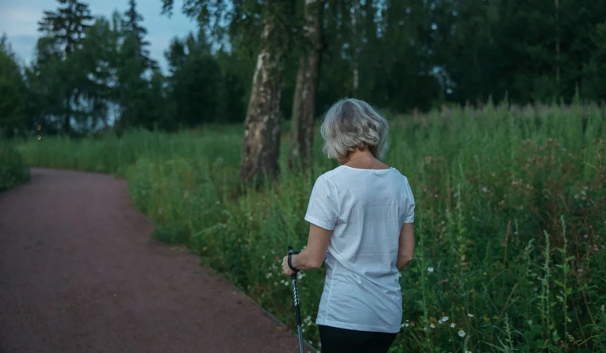 Elderly woman practicing Nordic walking on a park trail, promoting health and fitness.