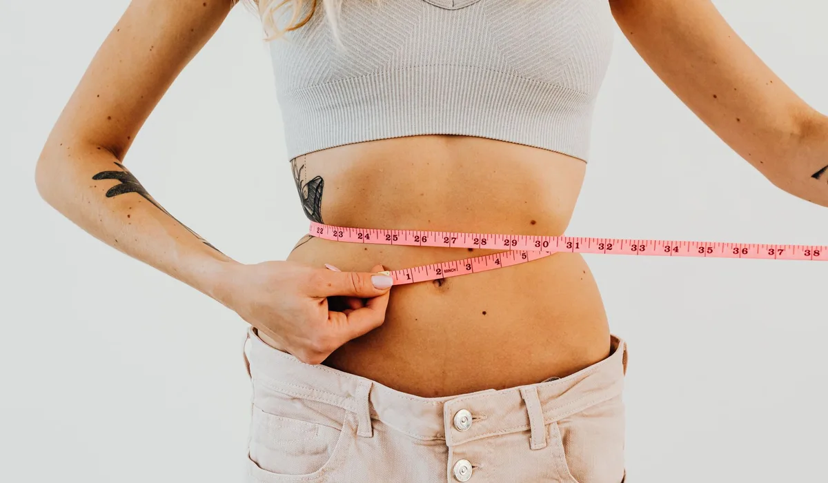 Close-up of woman in sports bra measuring waist with pink tape for fitness goals.
