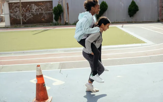 Side view of cheerful diverse teenage girls doing piggyback ride on sports ground during physical education class