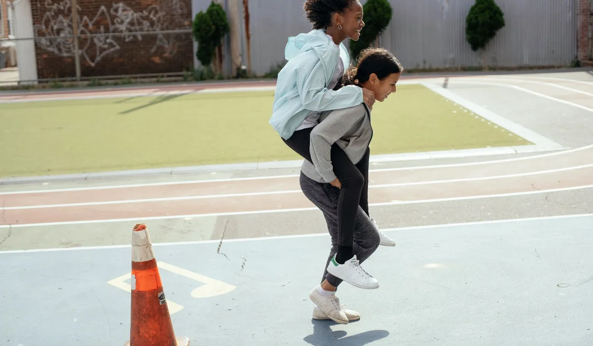 Side view of cheerful diverse teenage girls doing piggyback ride on sports ground during physical education class